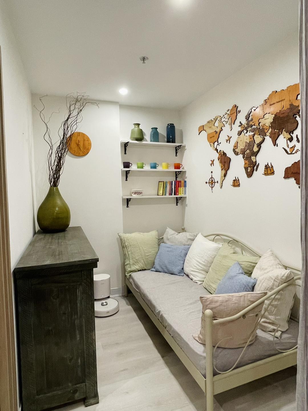 Compact eclectic bedroom with SCANDALINEN French linen on vintage iron daybed, wooden world map wall art and colourful shelf display