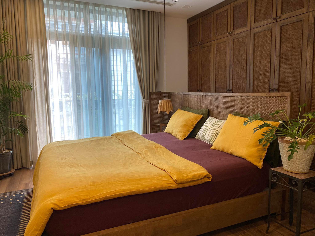 Mustard yellow SCANDALINEN French linen duvet cover and pillowcases on a rattan headboard bed with tropical plants