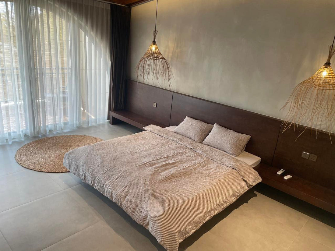 Grey stripe yarn-dyed SCANDALINEN French linen bedding in a resort-style bedroom with rattan pendants and low platform bed