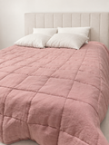Dusty pink French linen quilted blanket styled with ivory pillows in a bright studio bedroom